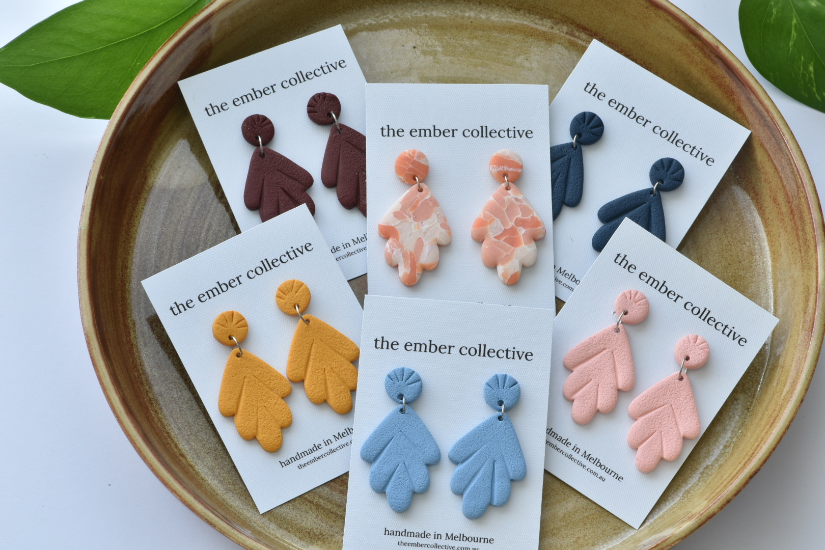 Handmade polymer clay earrings in warm colours, displayed on white cards in a handcrafted ceramic bowl